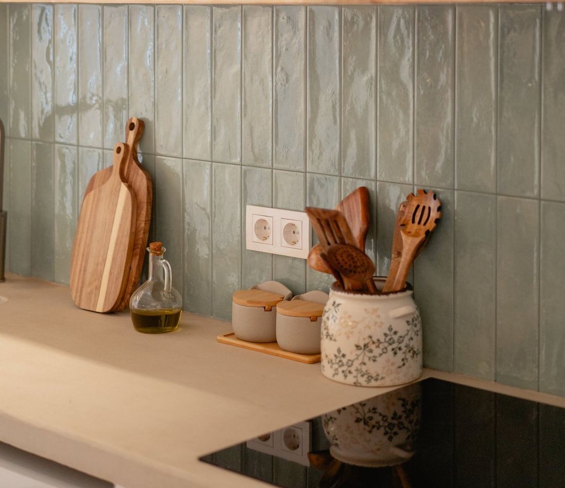 Detalle de la cocina: azulejo verde hecho a mano, tablas de madera, aceite y cucharas de madera.