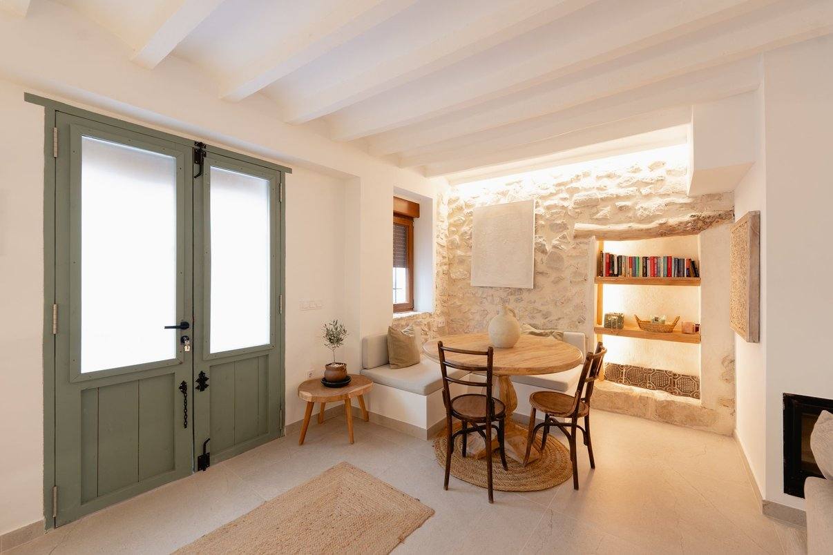 El salón junto a la puerta verde de dos hojas: banco de obra y mesa redonda junto a la piedra.